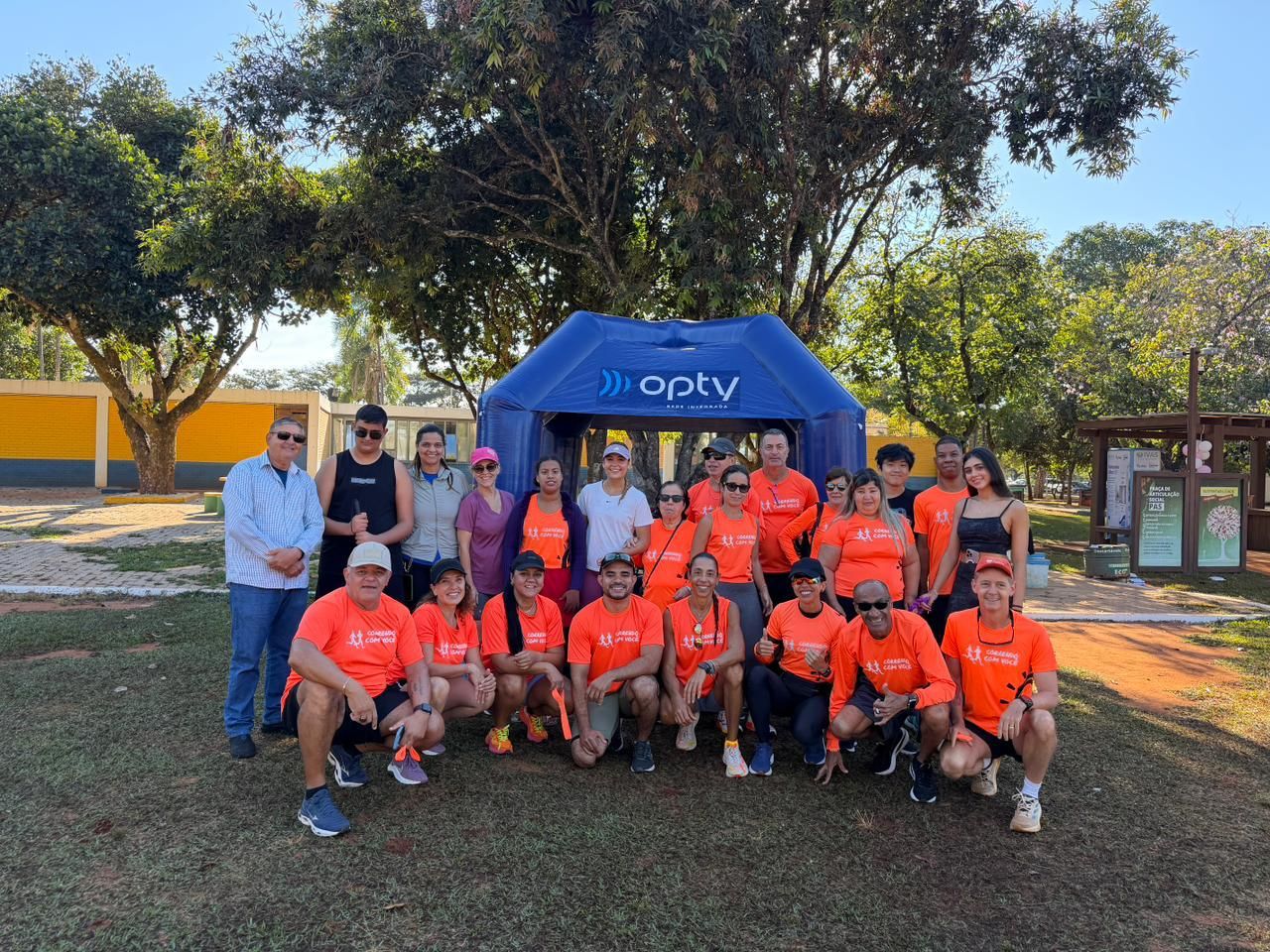 Grupo de integrantes do Correndo Com Você posando juntos embaixo de um arco inflável azul antes de uma corrida.