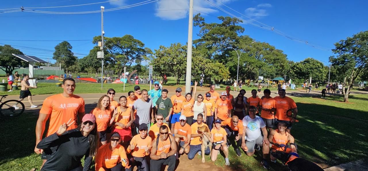 Grande grupo de integrantes do Correndo Com Você posando juntos em um parque em um dia ensolarado.
