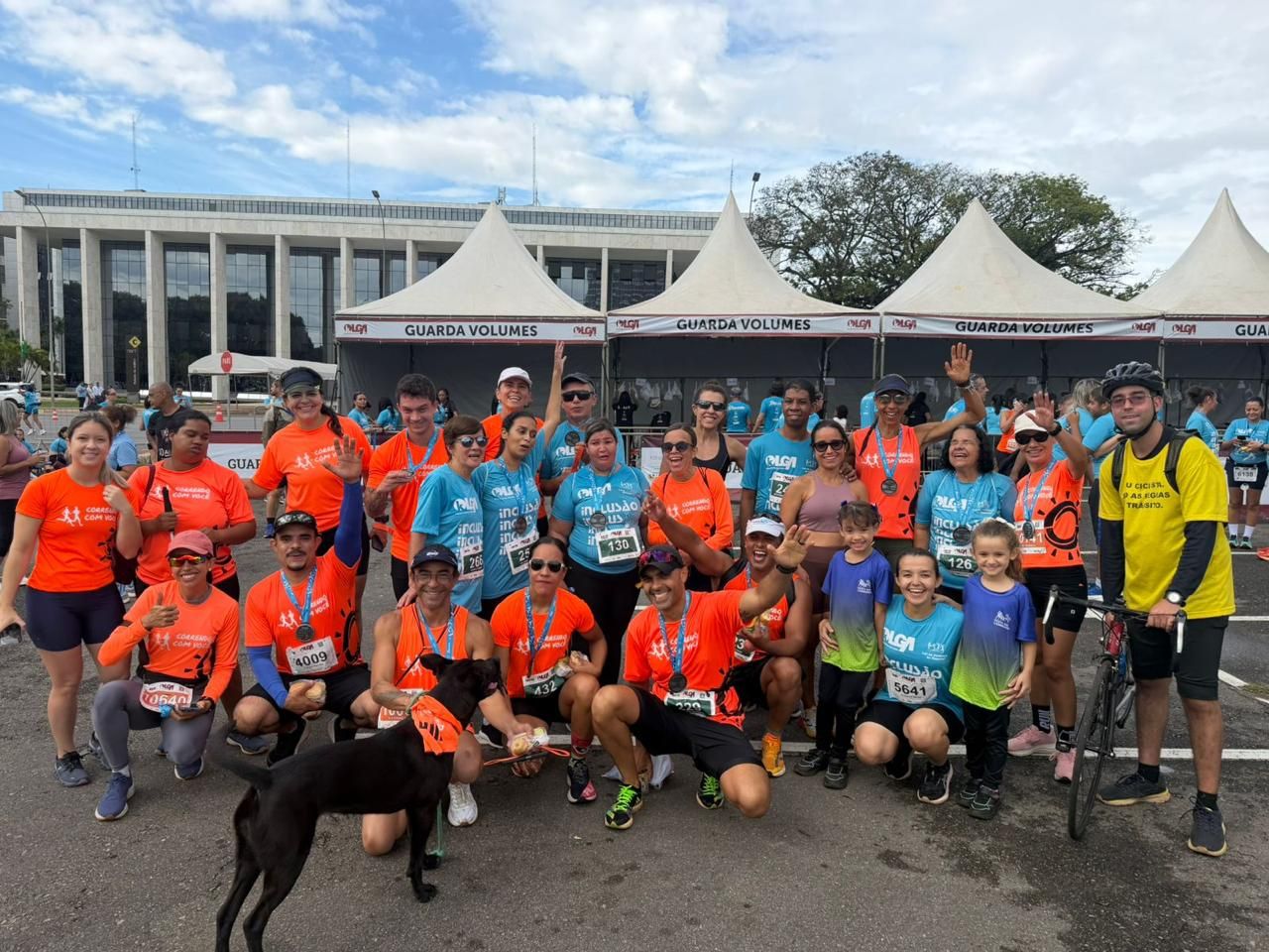 Grande grupo misto de corredores do Correndo Com Você e voluntários do evento posando juntos após uma corrida perto de um prédio público.