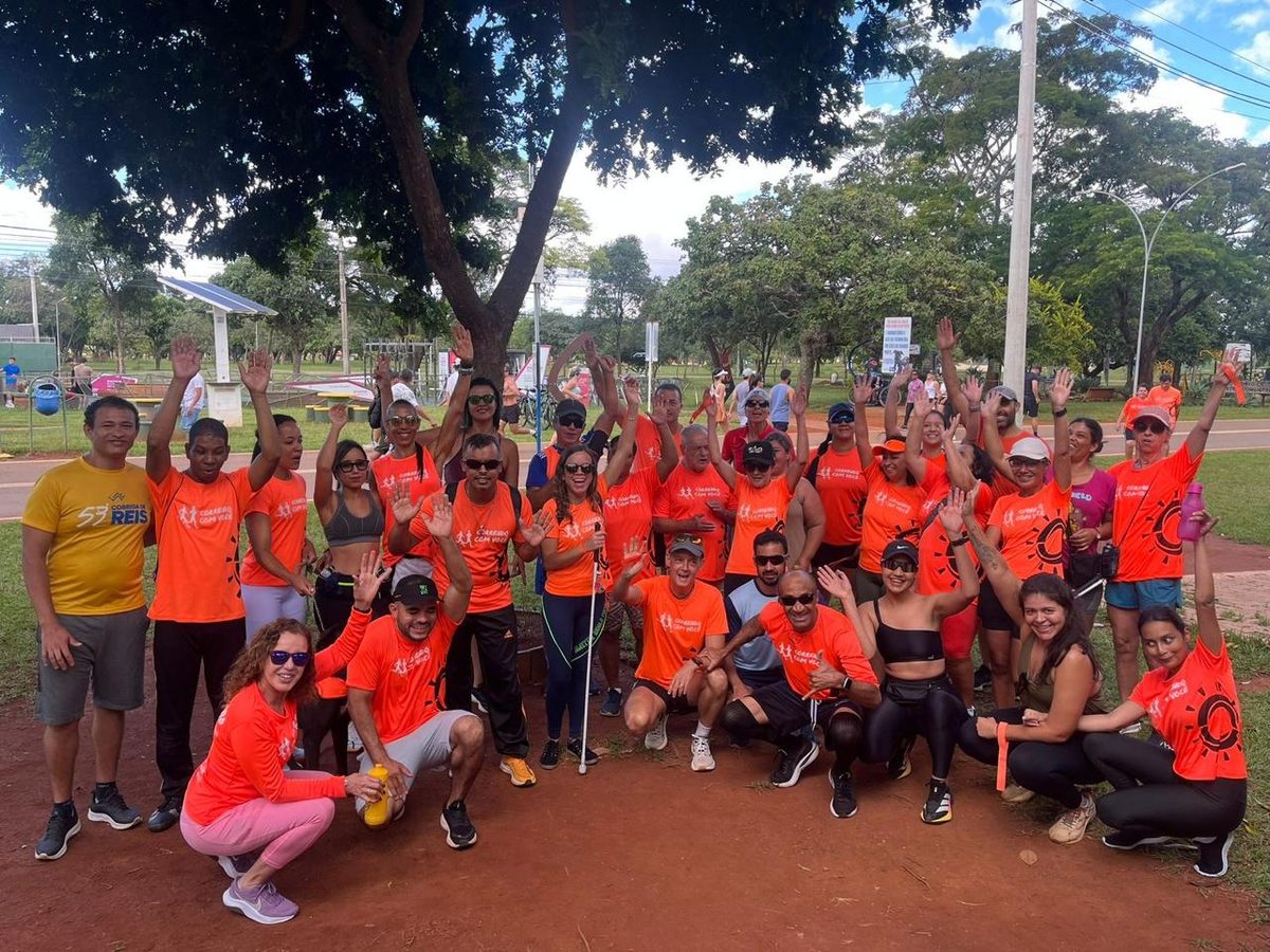 Grupo de corredores e guias do Correndo Com Você com camisetas laranjas iguais, comemorando juntos ao ar livre no Parque da Cidade.